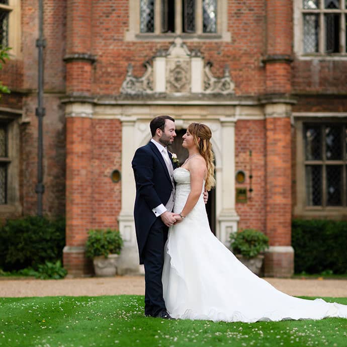 Newly wed couple gazing into each others eyes outside large manor house 